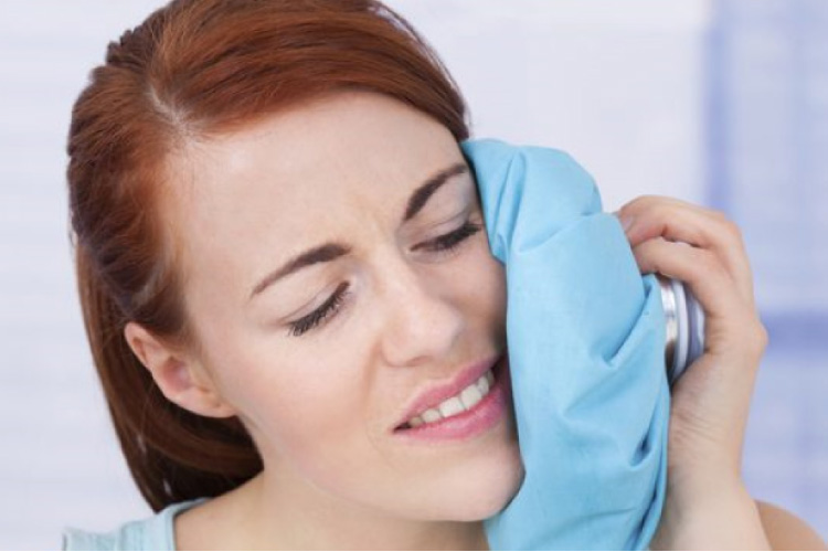 red headed woman applying an ice pack to her jaw after oral surgery