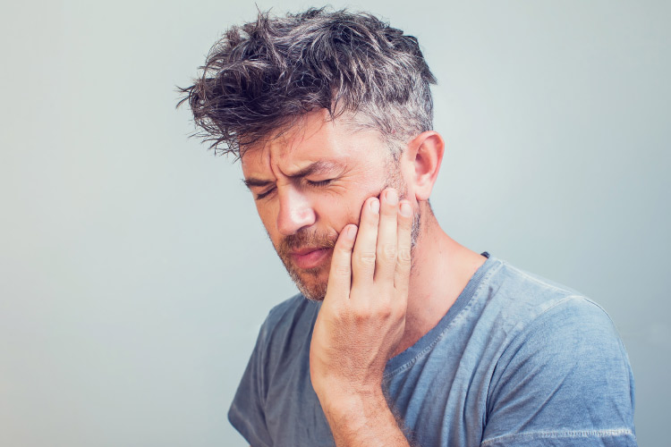 man with messy salt and pepper hair holding his jaw in pain after a dental emergency