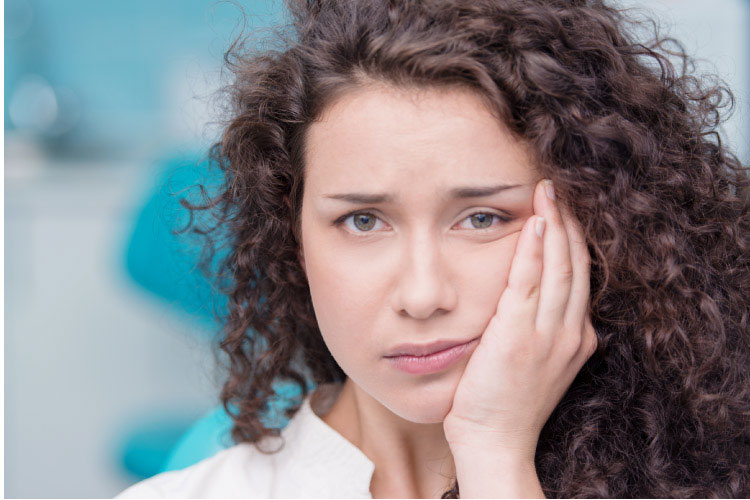 curly haired woman holding her jaw in pain because she needs a cavity filled