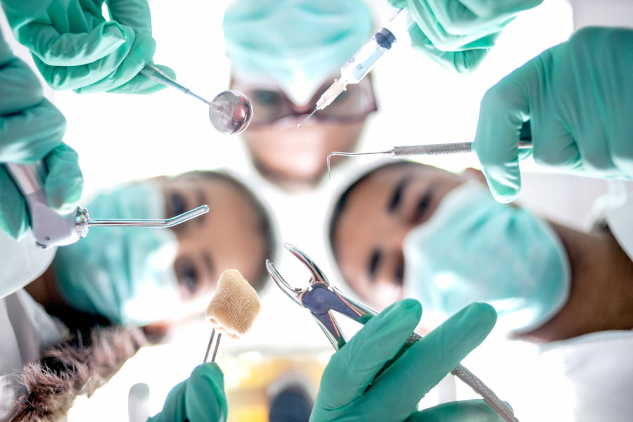 Masked dental professionals holding tools looking down on oral surgery patient