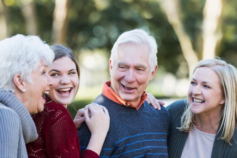 A senior couple laughing with their daughter and granddaughter outdoors