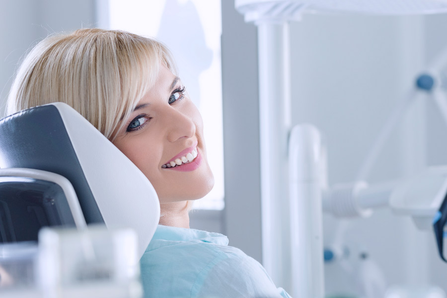 Smiling blonde woman with white teeth relaxing in the dental chair after teeth whitening treatment.